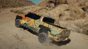 Kia Tasman con camuflaje multicolor sobre un camino de tierra entre las rocas de Alabama Hills