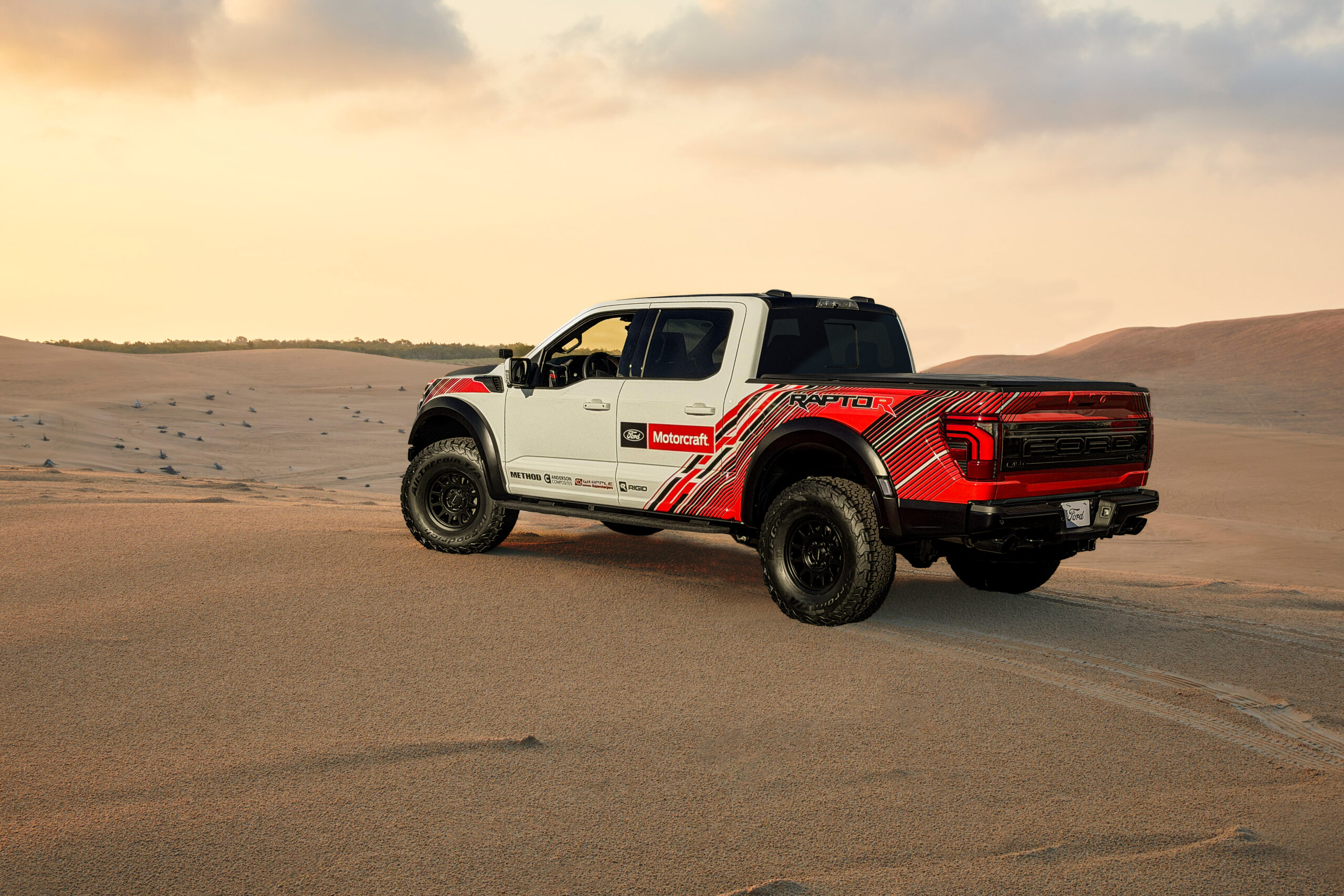 Vista tres cuartos trasera de la Ford F-150 Raptor R project vehicle en el desierto al atardecer.