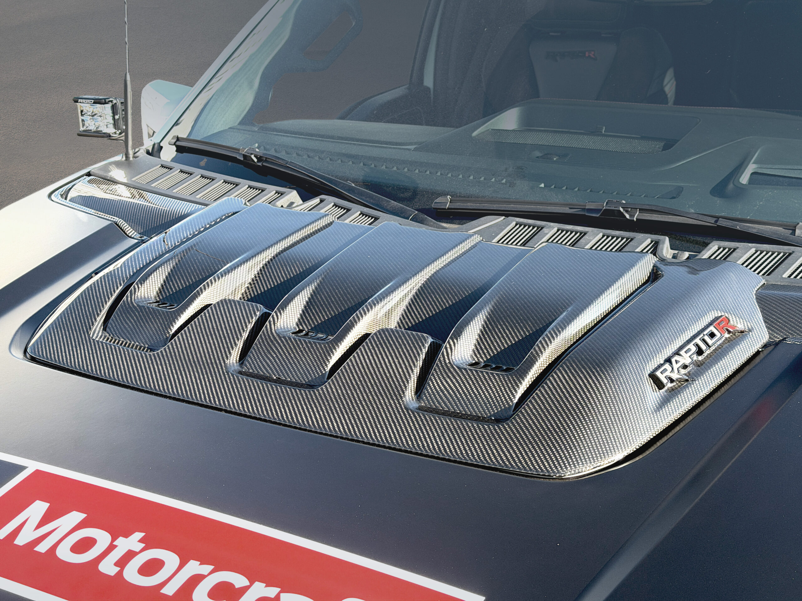 Primer plano del capó de la Ford F-150 Raptor R project vehicle, resaltando la toma de aire de fibra de carbono brillante y el logo RAPTOR R.