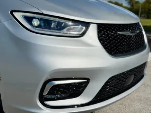 Detalle del faro delantero y la parrilla negra con el emblema alado de la Chrysler Pacifica Pinnacle