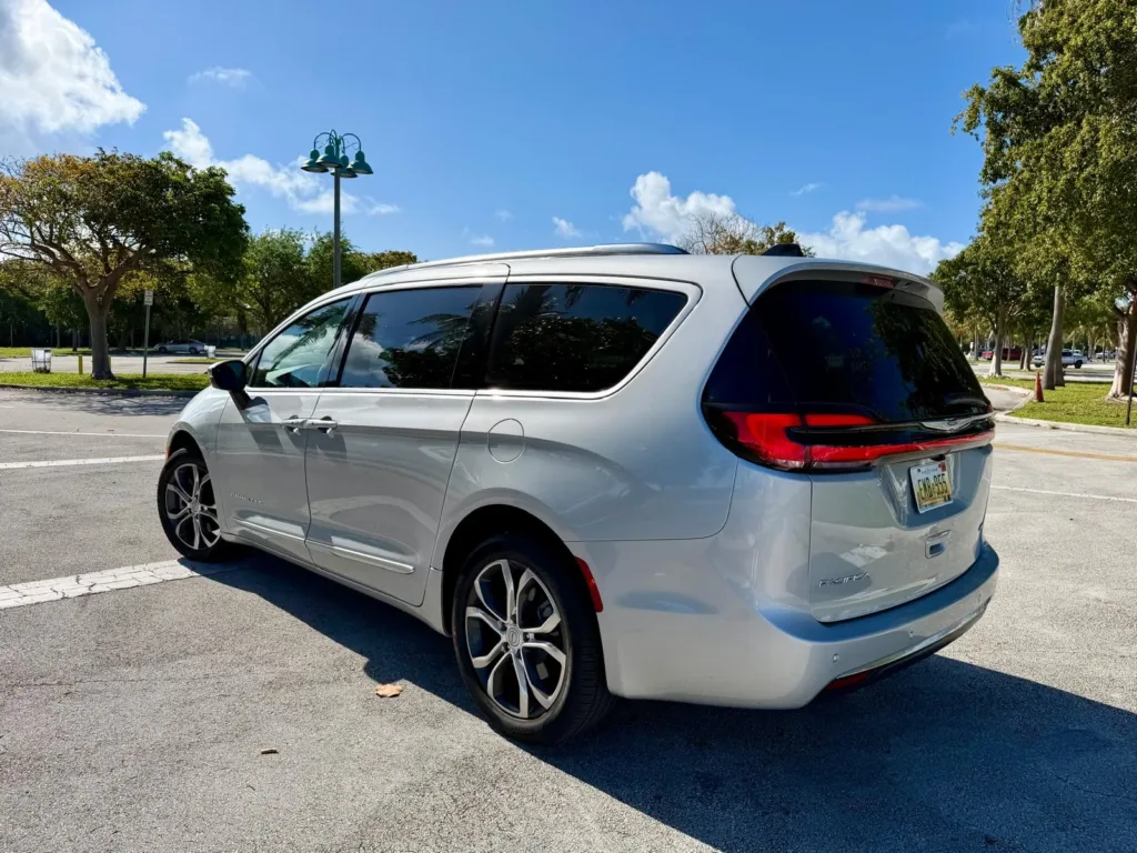 Chrysler Pacifica Pinnacle plateada en un estacionamiento arbolado, vista de tres cuartos trasera