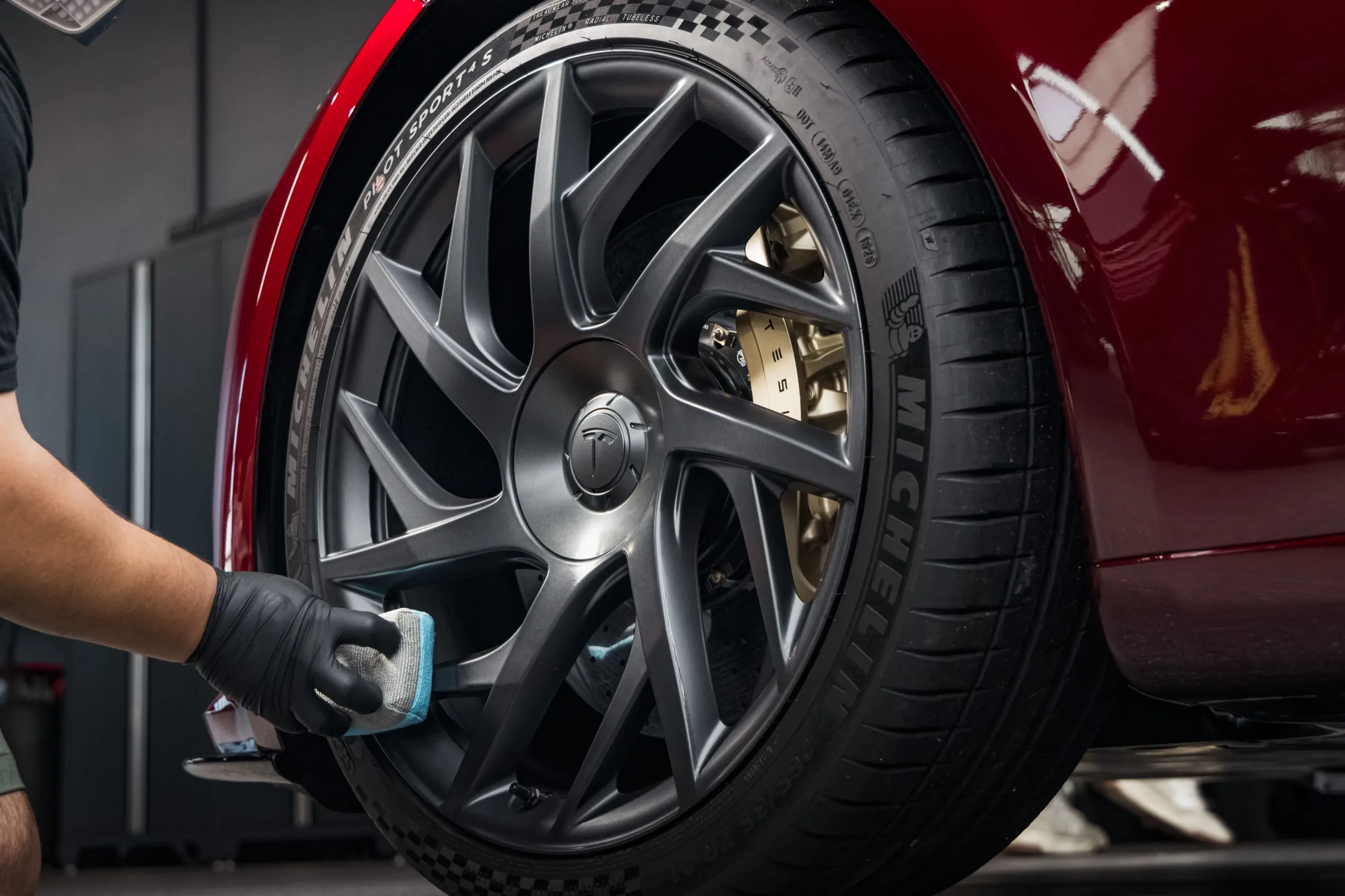 Mano con guante negro limpia la llanta gris de rayos finos del Model S rojo con un paño azul