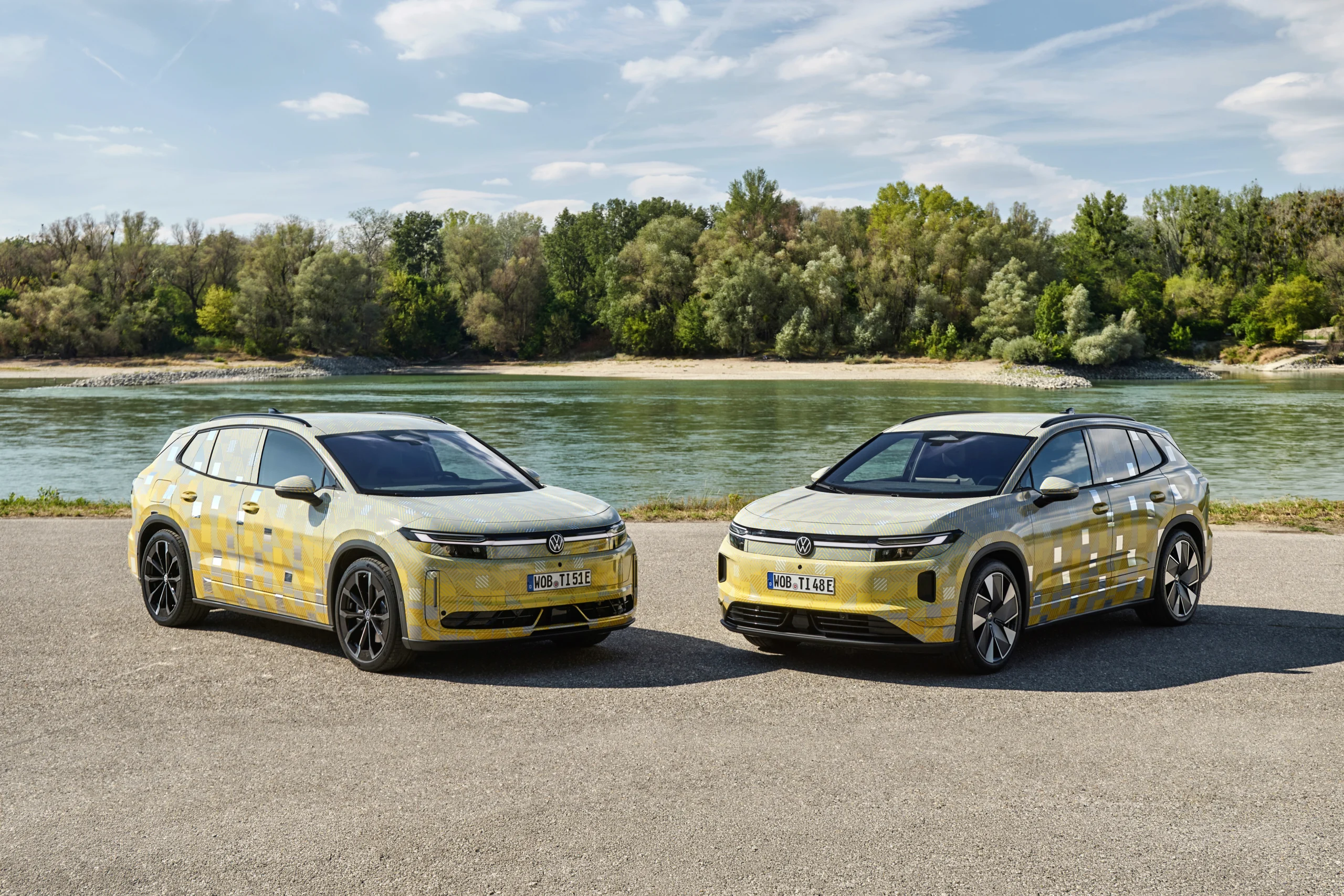 Dos prototipos camuflados de Volkswagen estacionados de frente junto a un río, con árboles detrás