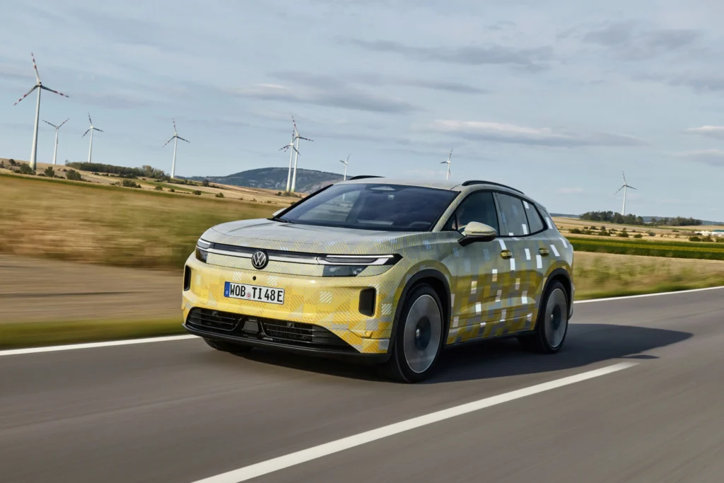 Prototipo camuflado del ID. Tiguan circulando por una carretera rural con aerogeneradores al fondo