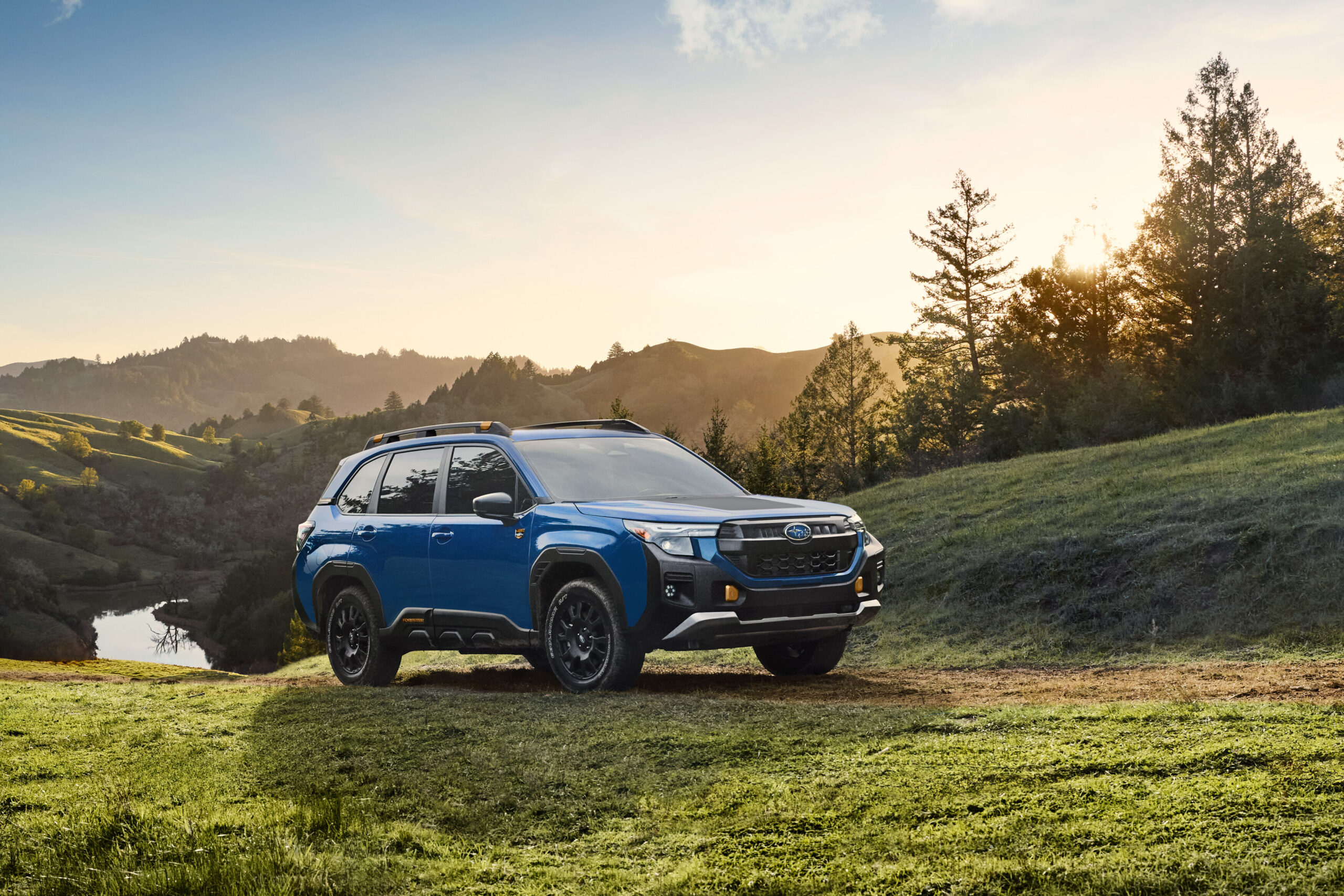 Subaru Forester Wilderness 2027 azul con detalles en cobre estacionado sobre un prado, con colinas y árboles al atardecer