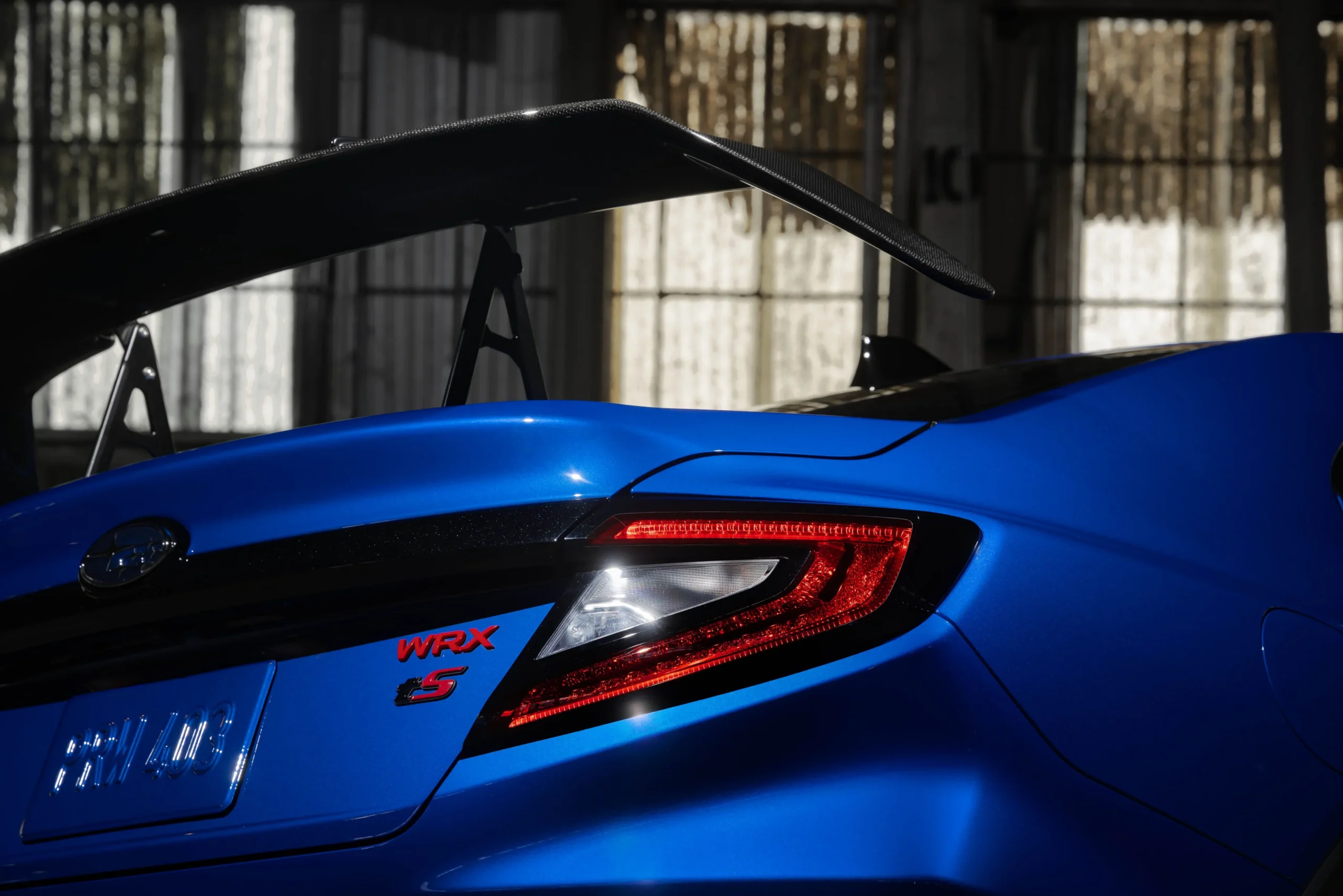 Subaru WRX azul con gran alerón trasero de carbono y luces traseras LED encendidas, vista posterior en detalle