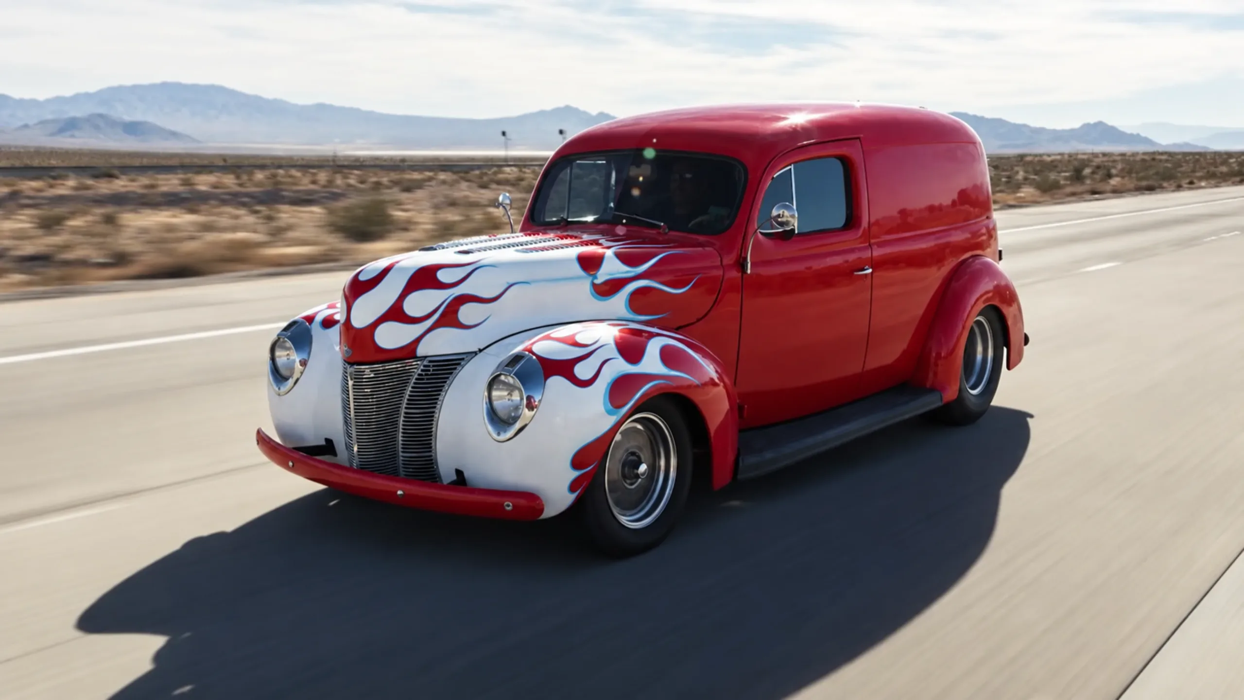 Furgoneta Ford Sedan Delivery roja con llamas blancas pintadas en una carretera del desierto