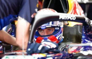Max Verstappen con el casco puesto, sentado en el cockpit de su Red Bull mientras un mecánico lo asiste
