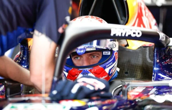 Max Verstappen con el casco puesto, sentado en el cockpit de su Red Bull mientras un mecánico lo asiste