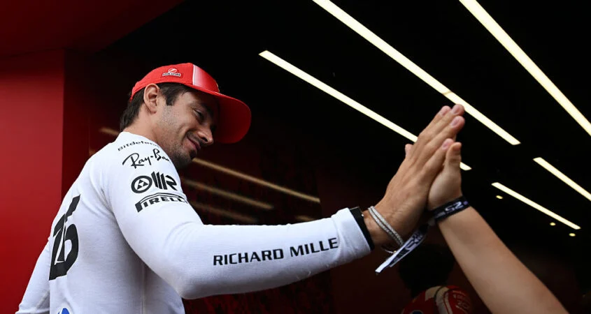 Charles Leclerc, con gorra roja de Ferrari, choca la mano con un integrante del equipo al entrar al garaje