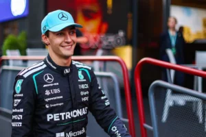 George Russell sonríe en el paddock con gorra celeste y el traje de carrera negro de Mercedes