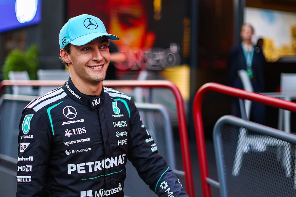 George Russell sonríe en el paddock con gorra celeste y el traje de carrera negro de Mercedes