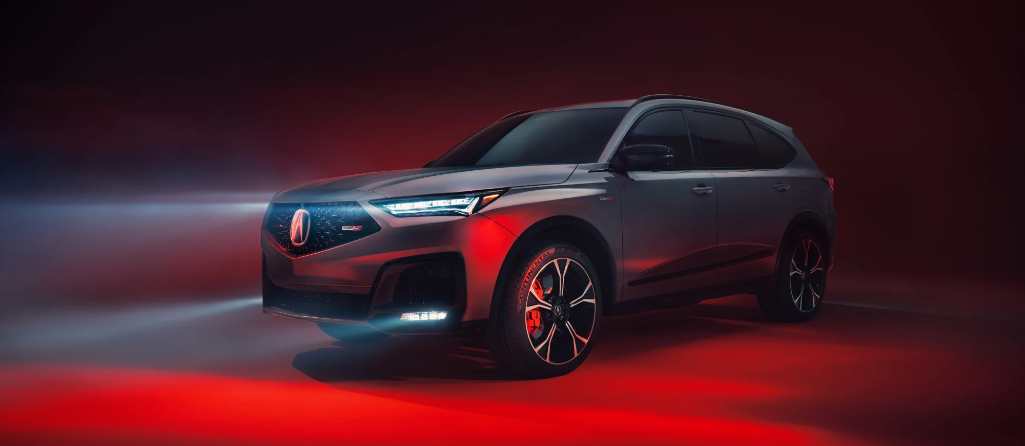 Acura MDX Type S gris con pinzas de freno rojas en un estudio con iluminación roja, vista de tres cuartos