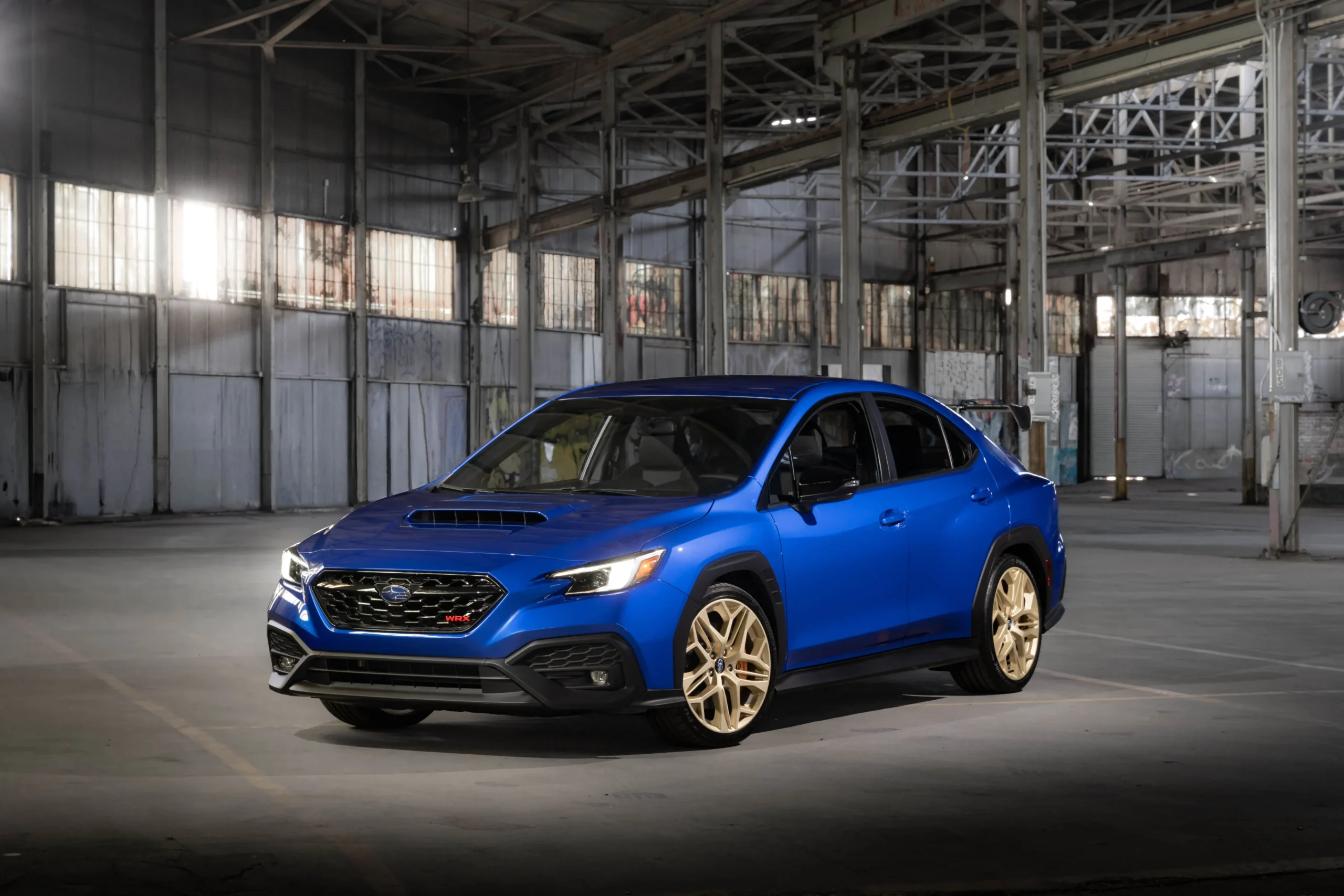 Subaru WRX GD25 2027 en World Rally Blue con llantas doradas, vista de tres cuartos delantera en una nave