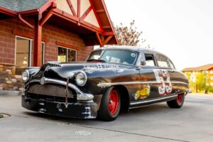 Hudson Hornet negro con ruedas rojas y el número de carrera en la puerta, uno de los autos de la caravana Ruta 66
