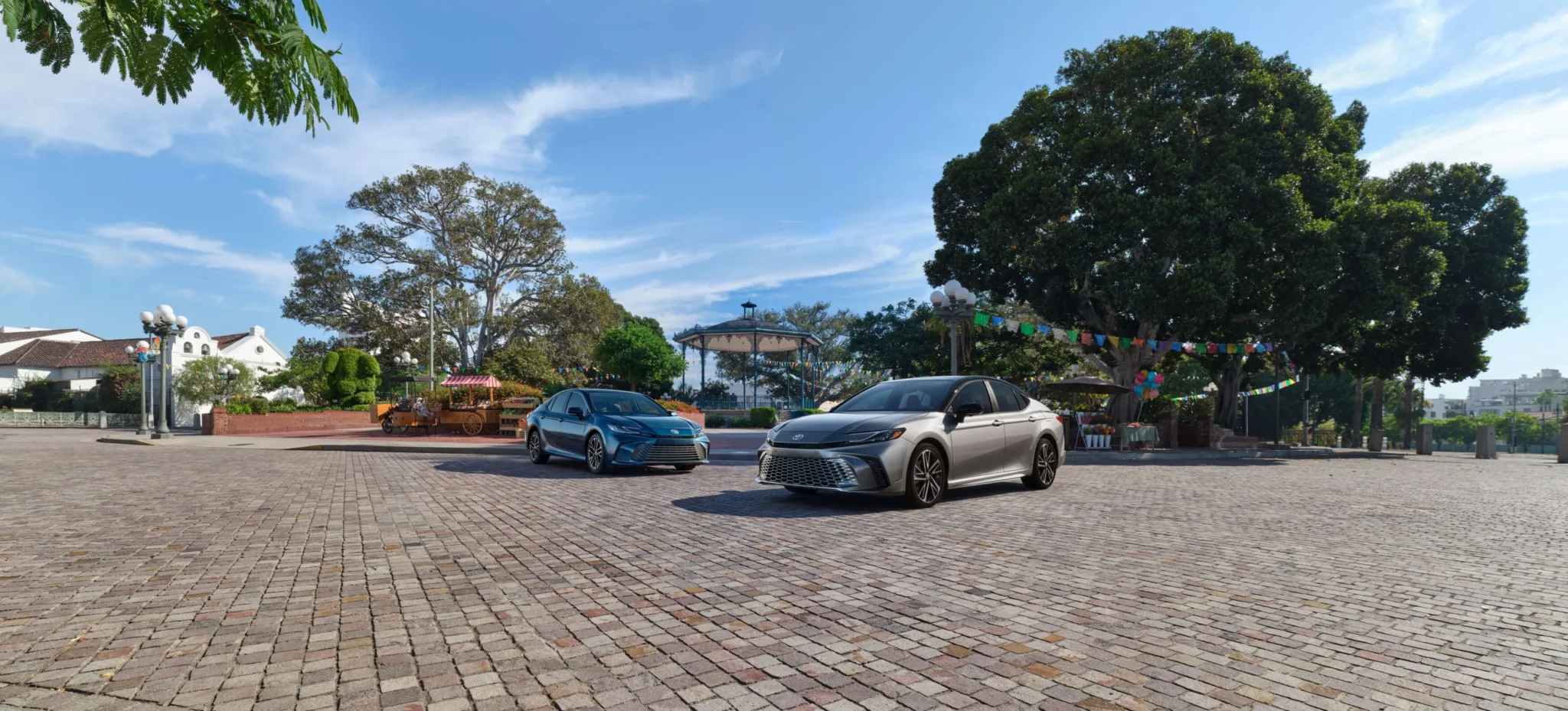 Dos Toyota Camry 2027 estacionados lado a lado en una plaza adoquinada con árboles