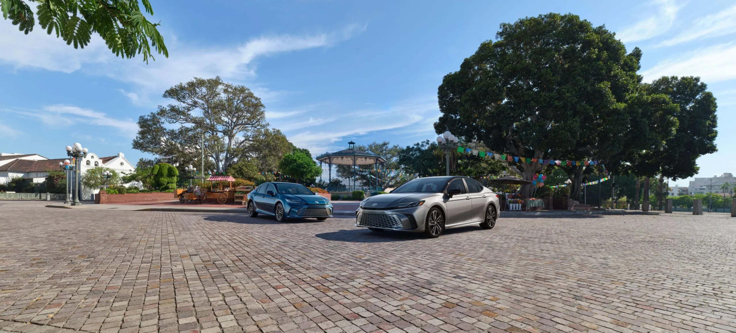 Dos Toyota Camry 2027 estacionados lado a lado en una plaza adoquinada con árboles