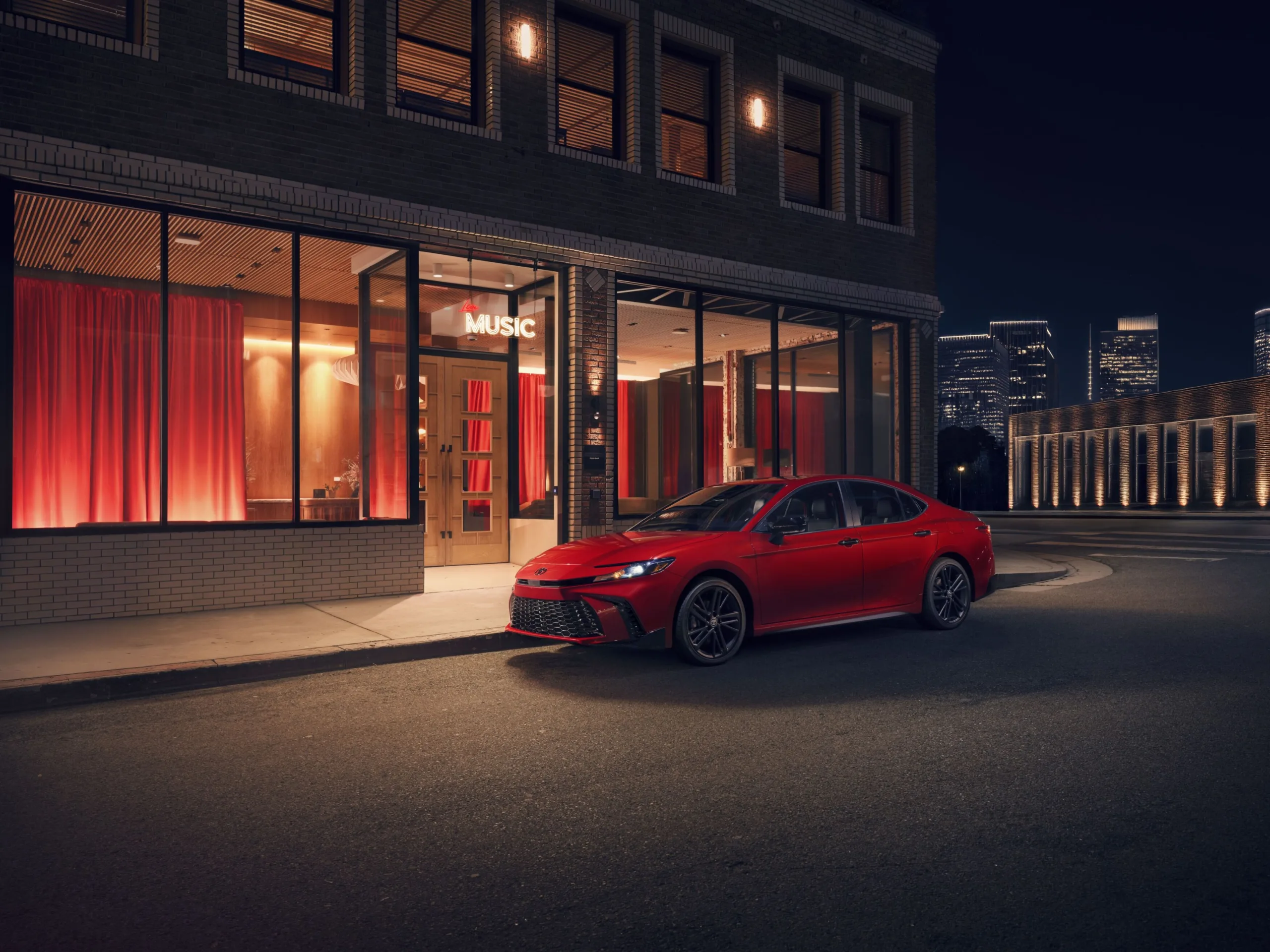 Toyota Camry Nightshade 2027 rojo estacionado de noche frente a un edificio iluminado