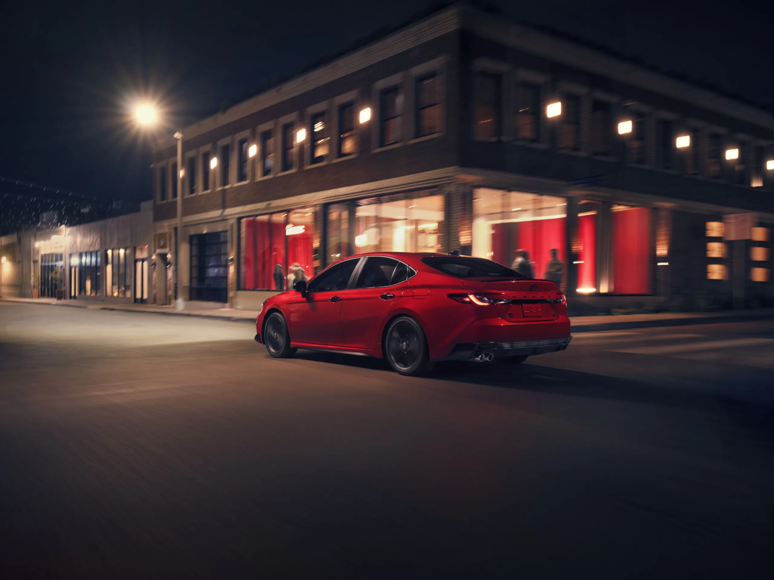 Toyota Camry Nightshade 2027 rojo visto de atrás y de costado en una calle de noche