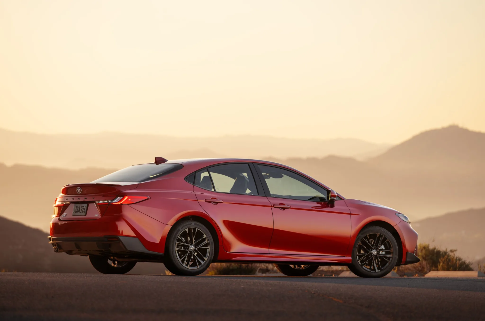 Toyota Camry SE 2027 rojo visto de costado al atardecer, con colinas de fondo