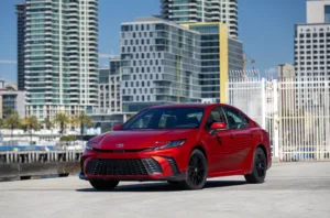 Toyota Camry 2027 SE rojo (Supersonic Red) visto de frente en una calle con edificios altos al fondo