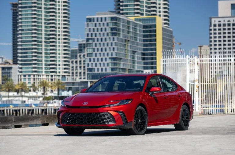 Toyota Camry 2027 SE rojo (Supersonic Red) visto de frente en una calle con edificios altos al fondo