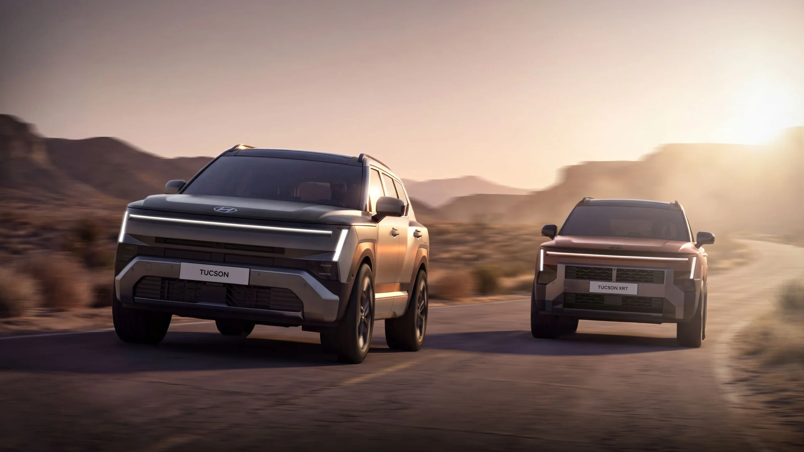 Nuevo Hyundai Tucson gris y Tucson XRT cobrizo circulando por una carretera del desierto al atardecer