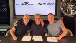 Firma del acuerdo entre AC Schnitzer y AM Group: tres directivos sonríen tras una mesa con los documentos