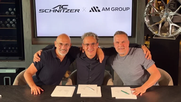 Firma del acuerdo entre AC Schnitzer y AM Group: tres directivos sonríen tras una mesa con los documentos