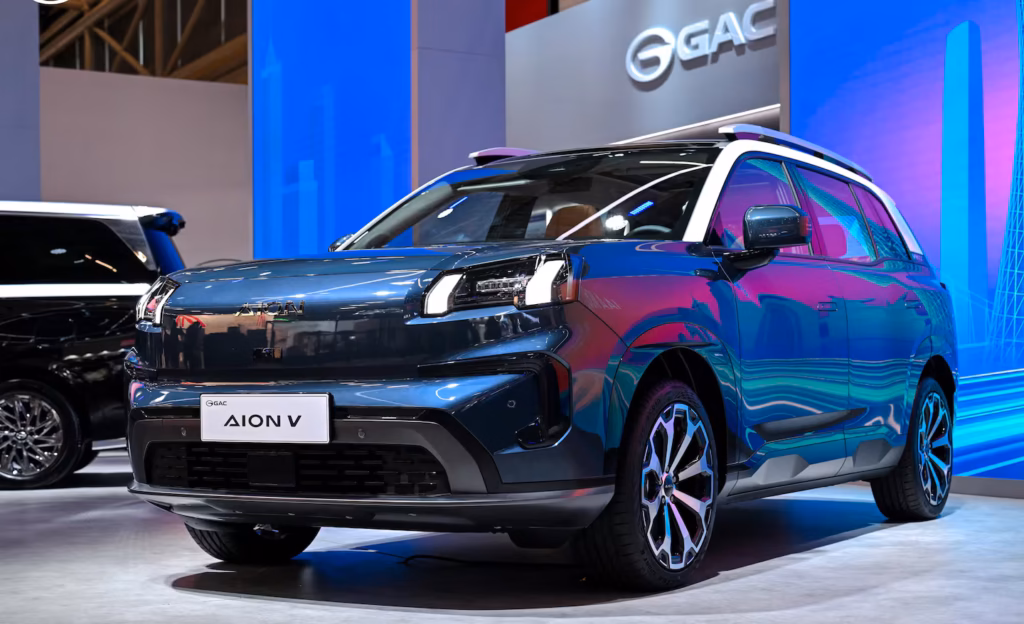 Aion V azul exhibido en el stand de GAC durante un salón del automóvil, vista de tres cuartos delantera