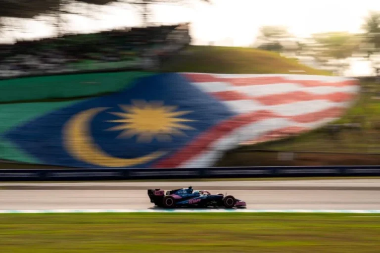 Un Alpine rueda en seco frente a la bandera de Malasia pintada en la ladera; el pronóstico anticipa lluvia en Sepang