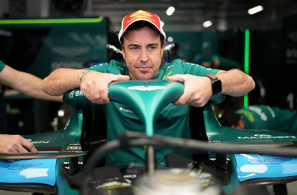 Fernando Alonso, con polo verde de Aston Martin, se apoya en el halo de su monoplaza dentro del garaje