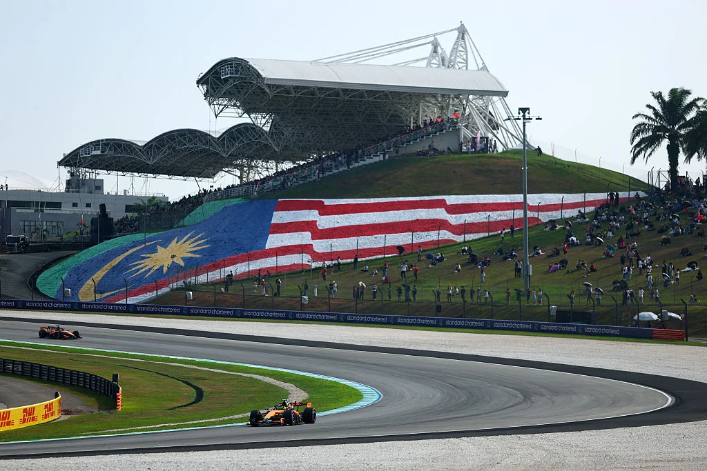 Dos McLaren recorren una curva de Sepang junto a la ladera con la bandera de Malasia pintada y aficionados
