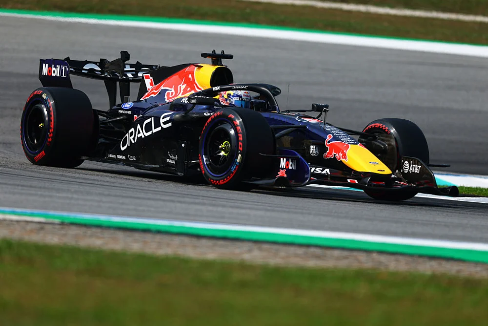 Monoplaza de Red Bull en pista junto al pianito verde y blanco, con el pasto en primer plano