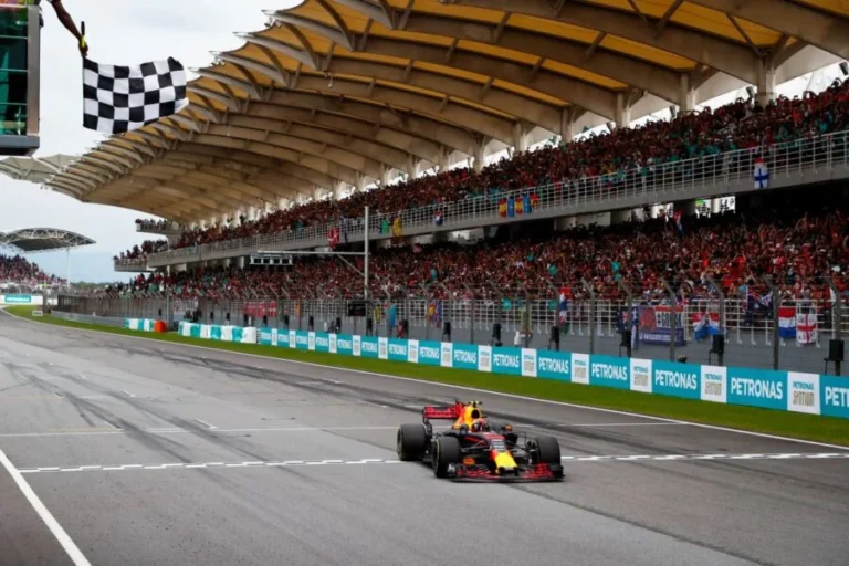 Max Verstappen cruza la meta con su Red Bull bajo la bandera a cuadros en el circuito de Sepang, ante tribunas llenas