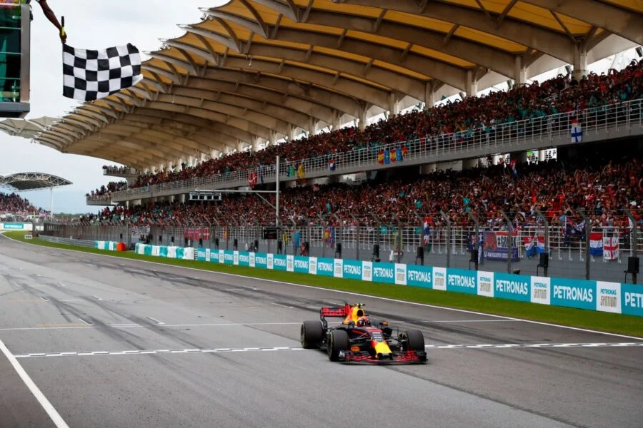 Max Verstappen cruza la meta con su Red Bull bajo la bandera a cuadros en el circuito de Sepang, ante tribunas llenas