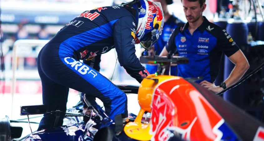 Piloto de Red Bull se sube a su monoplaza en el garaje mientras un mecánico del equipo observa
