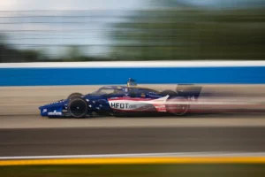 Monoplaza número 14 de AJ Foyt Racing con los colores de HFOT, a toda velocidad en un óvalo de IndyCar