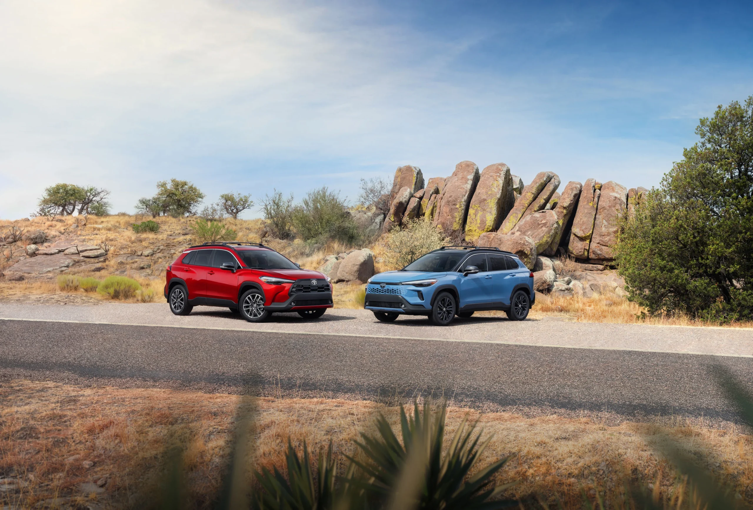 Toyota Corolla Cross 2027 rojo y Corolla Cross Hybrid azul en una carretera junto a grandes rocas