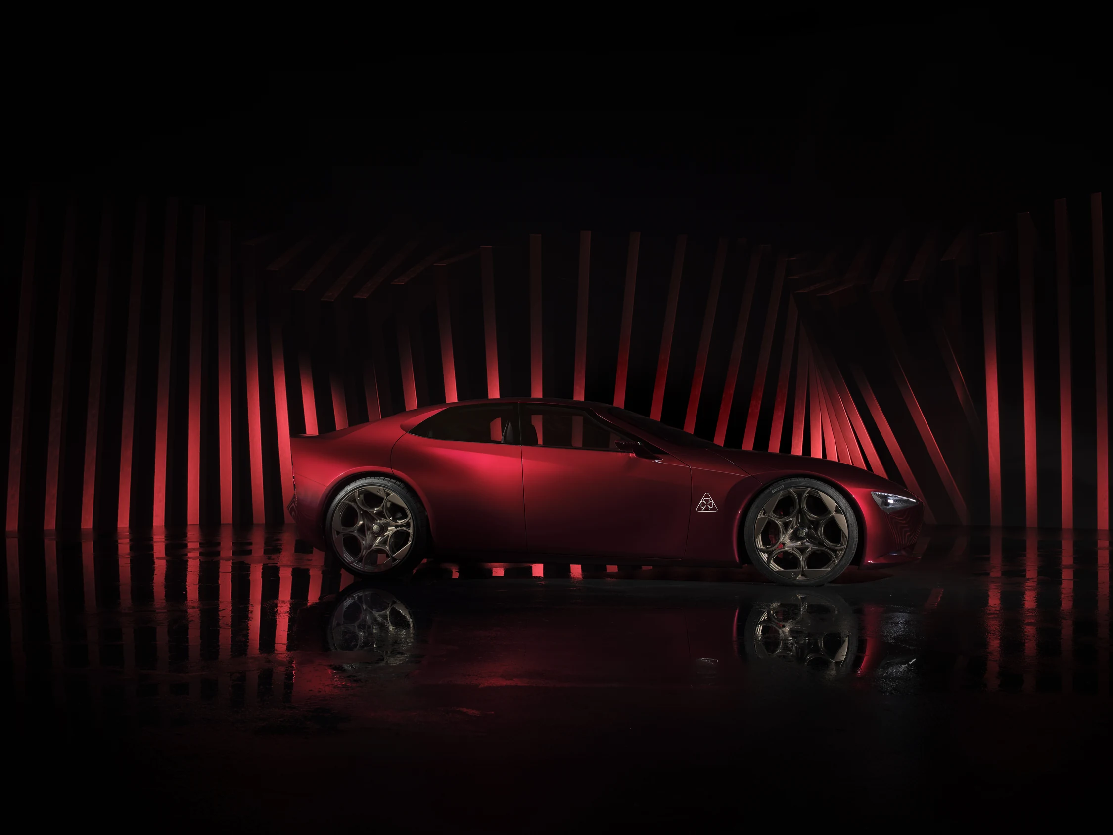 Alfa Romeo Cuorerosso de perfil, un coupé rojo con llantas doradas sobre un fondo de franjas rojas