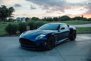 Aston Martin DB12 S 2026 azul visto de frente y de costado al atardecer, con llantas negras y la parrilla grande