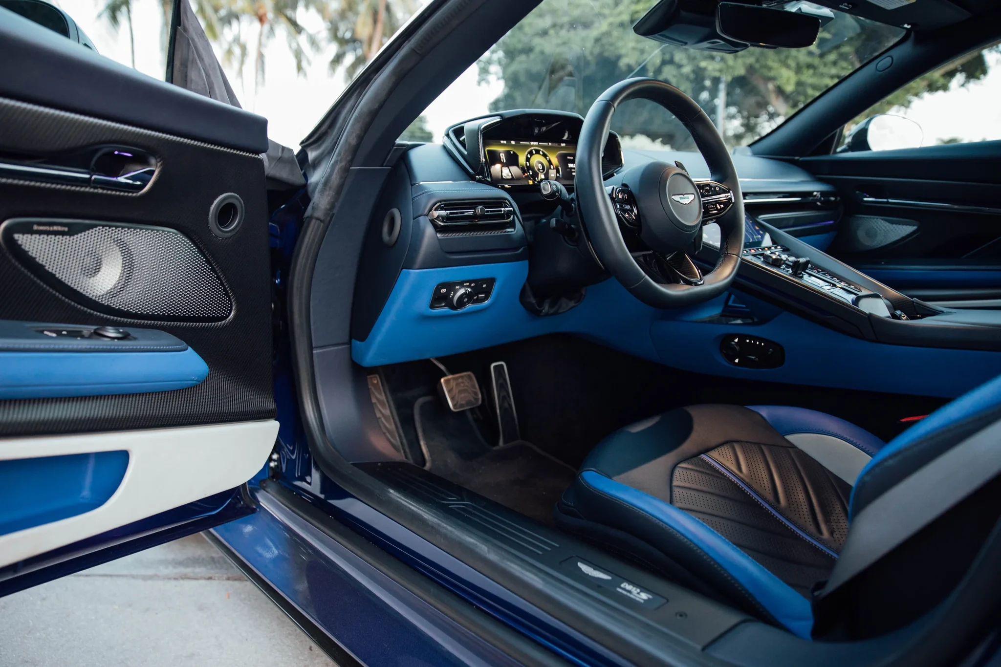 Interior del Aston Martin DB12 S visto desde la puerta abierta, con el volante y el tablero azul