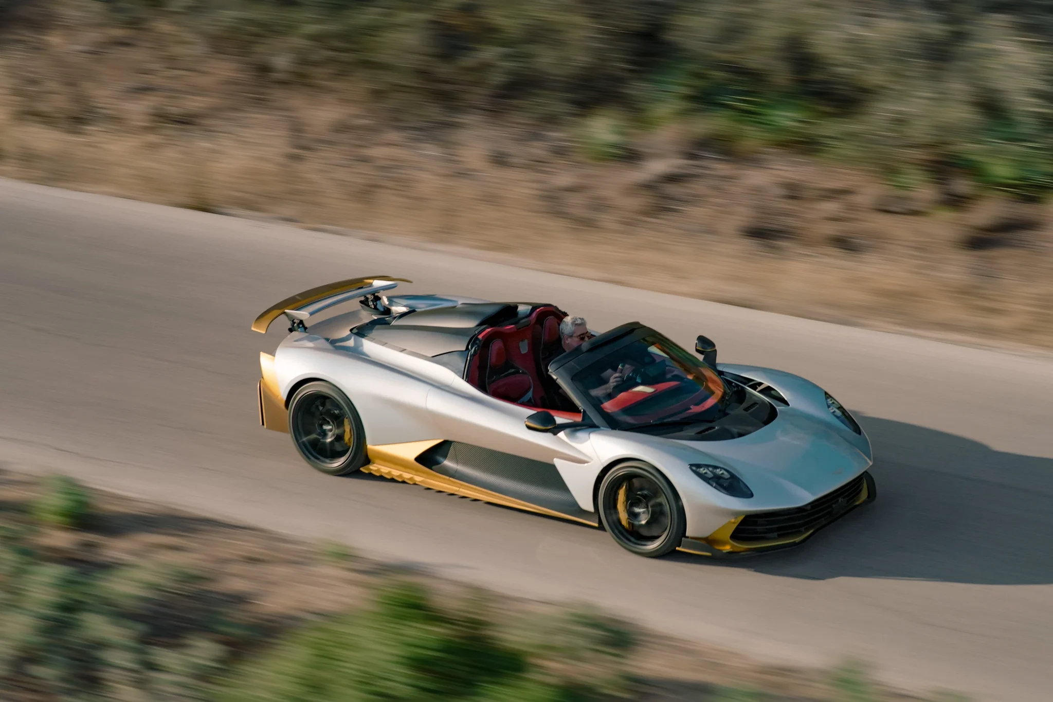 Aston Martin Valhalla Spider de lado en una curva de carretera, con el conductor al volante