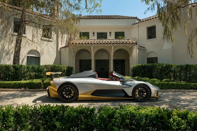 Aston Martin Valhalla Spider visto de perfil, sin techo, con el alerón trasero levantado, frente a una casa