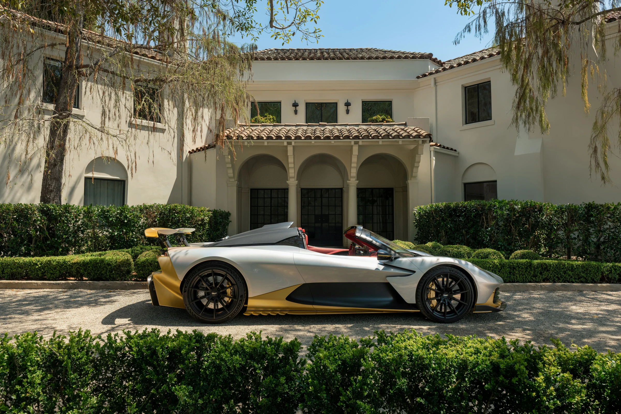 Aston Martin Valhalla Spider visto de perfil, sin techo, con el alerón trasero levantado, frente a una casa