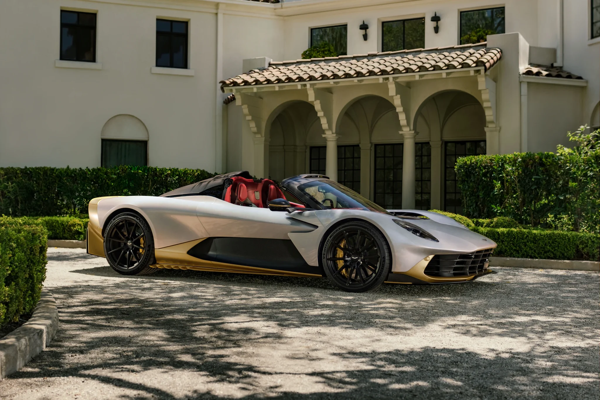 Perfil del Aston Martin Valhalla Spider con rines negros y faldones dorados, estacionado frente a una casa