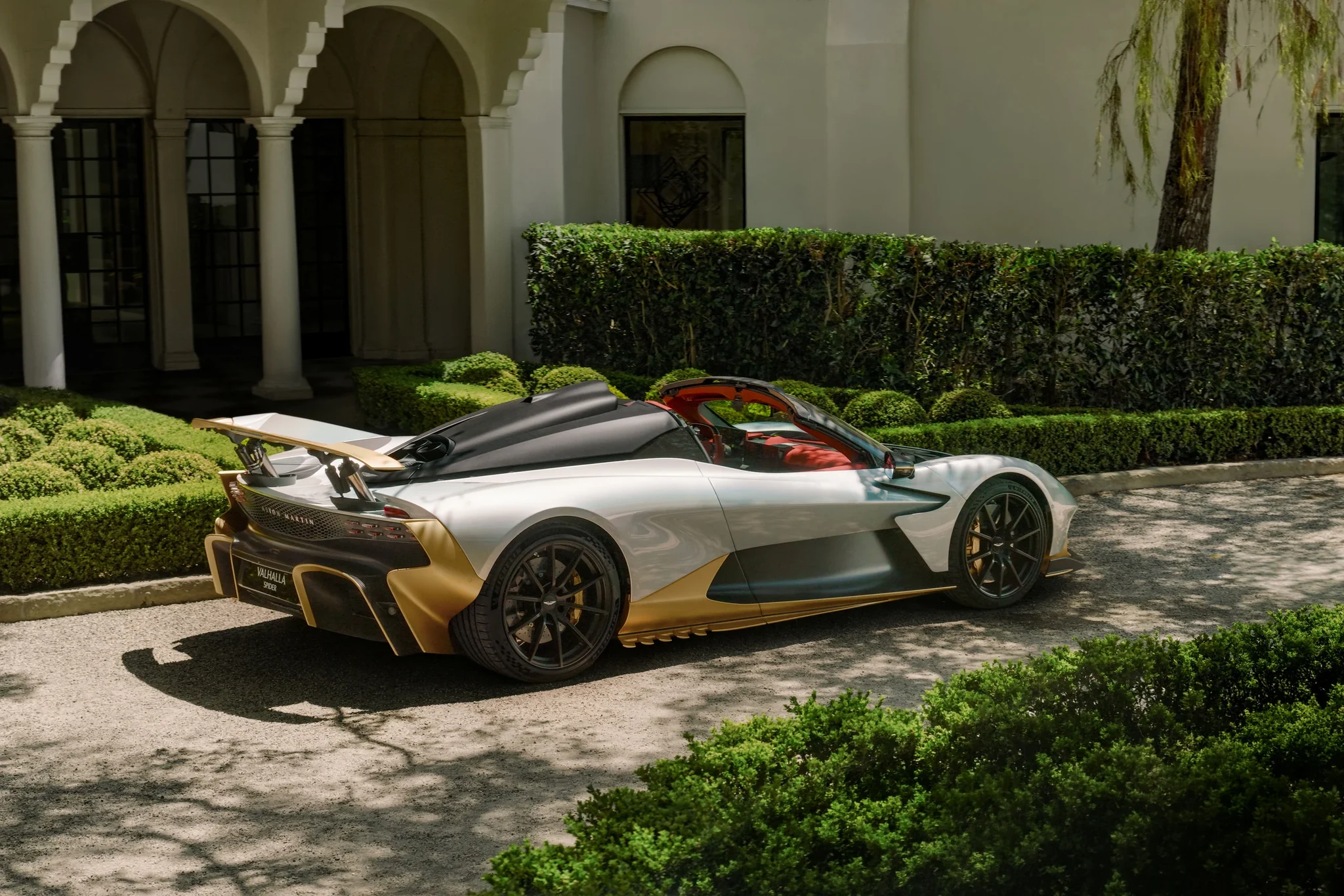 Aston Martin Valhalla Spider de tres cuartos traseros, con el alerón levantado, junto a una casa con arcos