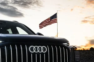 Audi Q9 negro con la parrilla iluminada frente a una bandera de Estados Unidos al atardecer, por la planta de Audi en Georgia