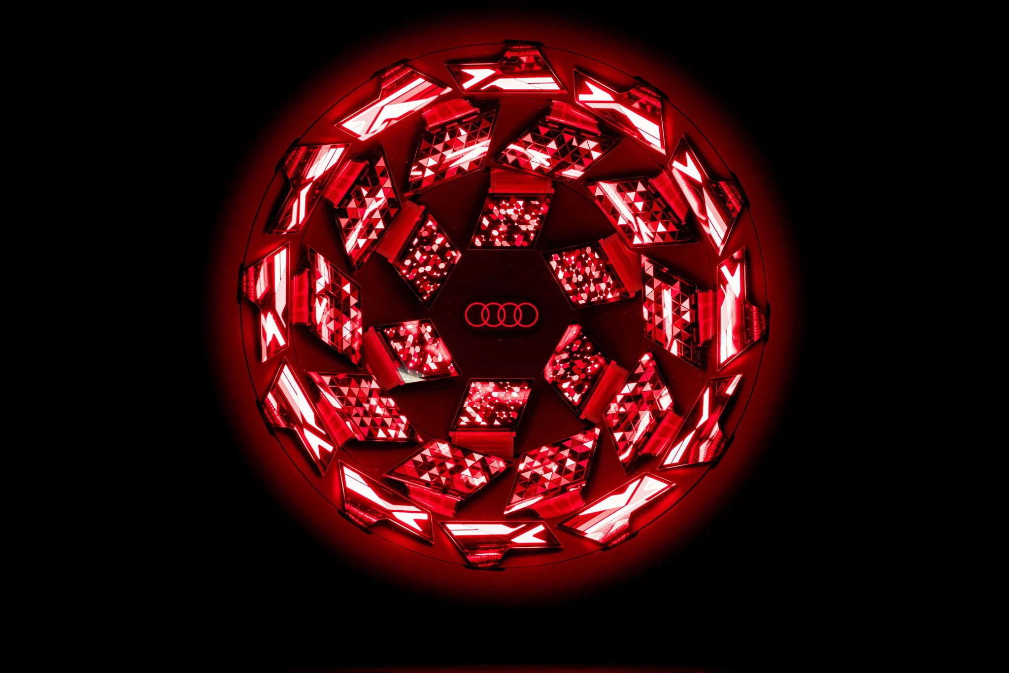 Luz OLED circular de Audi con el logo de los cuatro aros en el centro, encendida en rojo sobre fondo negro
