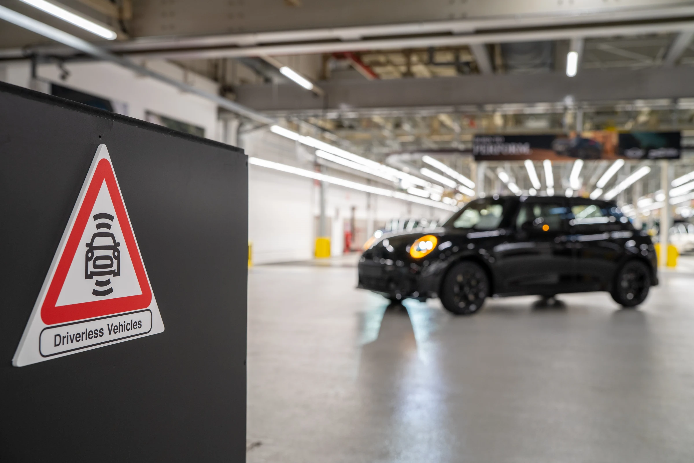 Cartel de advertencia de vehículos sin conductor junto a un MINI negro en la planta de MINI en Oxford